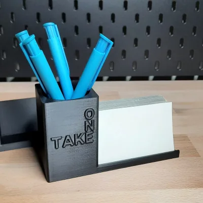 Die TAKE-ONE-Variante von vorn, vier blaue Stifte im Becher, weiße Karten in der Ablage