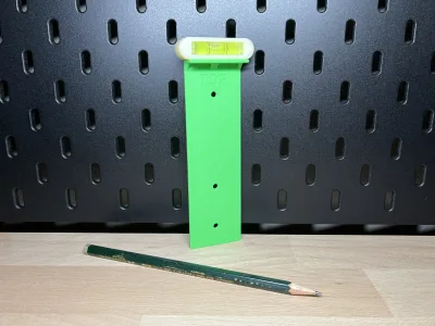 The green drilling template with a spirit level on the pegboard, a pencil beside it